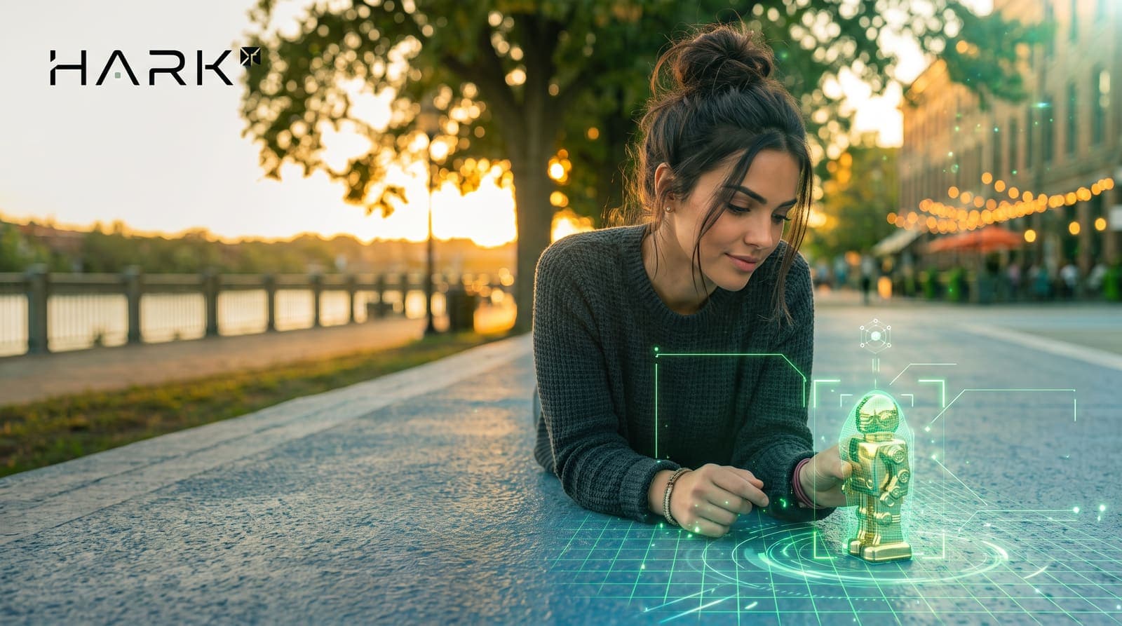 A woman lying on a riverside promenade at sunset studies a small gold robot figure wrapped in a green holographic scan overlay, with the Hark wordmark in the corner.